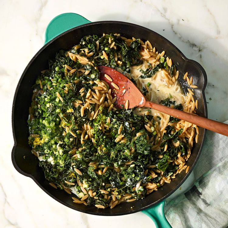 Overhead view of creamy whole-wheat orzo with wilted kale, scallions, dill and lemon zest in a cast-iron skillet