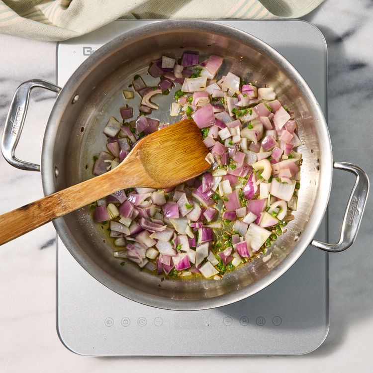 Diced red onion and serrano sweating in olive oil with cumin seeds in a stainless skillet