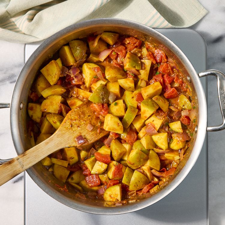 Yukon Gold potato chunks coated in tomato and spice mixture in a stainless skillet, ready for broth